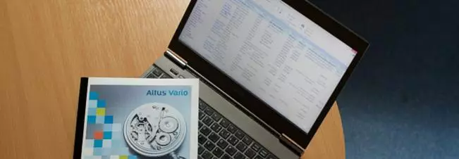 Notebook s otevřeným systémem Altus Vario vedle brožury s motivem hodinového strojku.