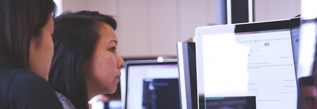 Dvě ženy pracují u počítače a společně sledují obsah na monitoru.