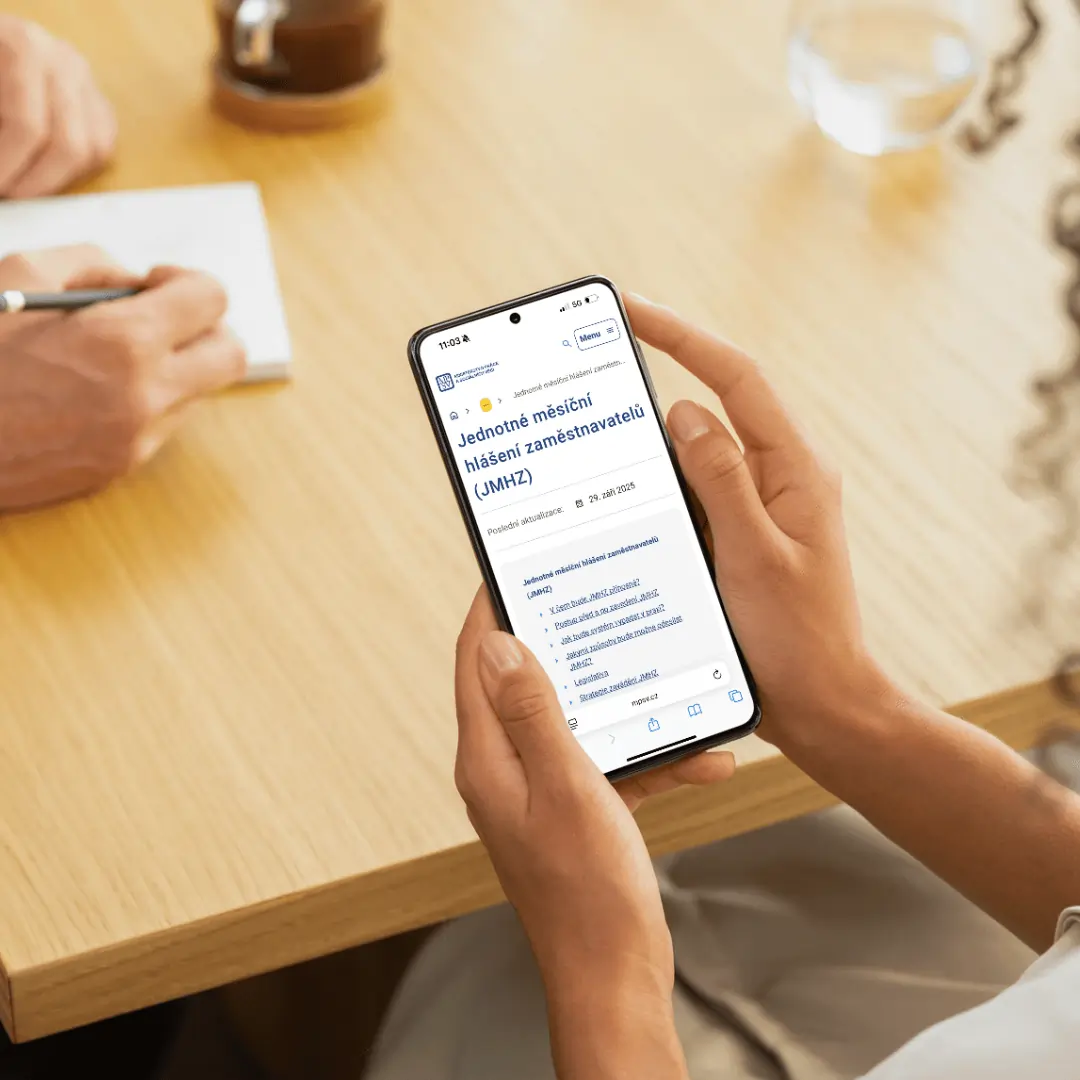 Osoba drží mobilní telefon se zobrazenou stránkou Jednotného měsíčního hlášení zaměstnavatelů (JMHZ).