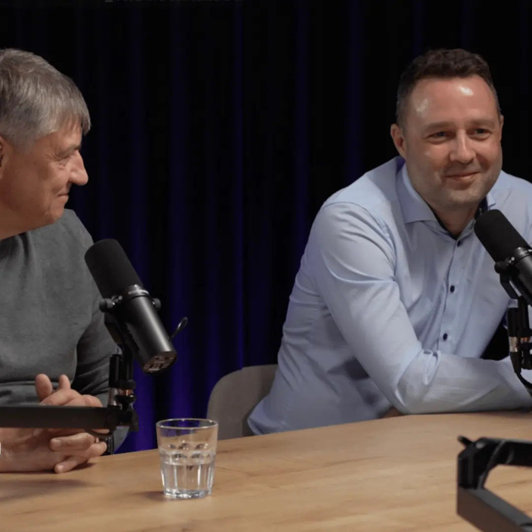 Dva muži diskutují u stolu během natáčení podcastu s mikrofony.